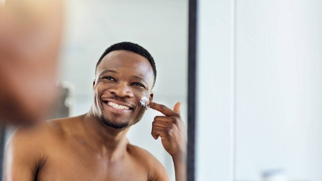 Homem aplicando hidratante no rosto para evitar os efeitos do tempo seco.