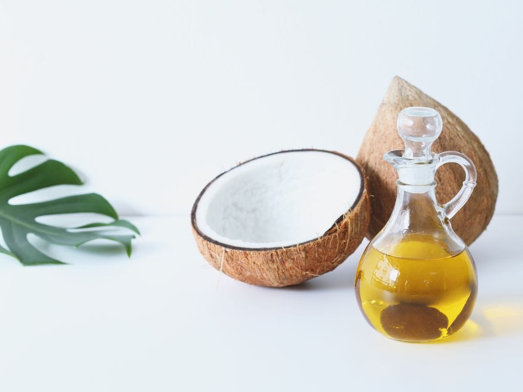 coco partido as meio e um recipiente com óleo de coco