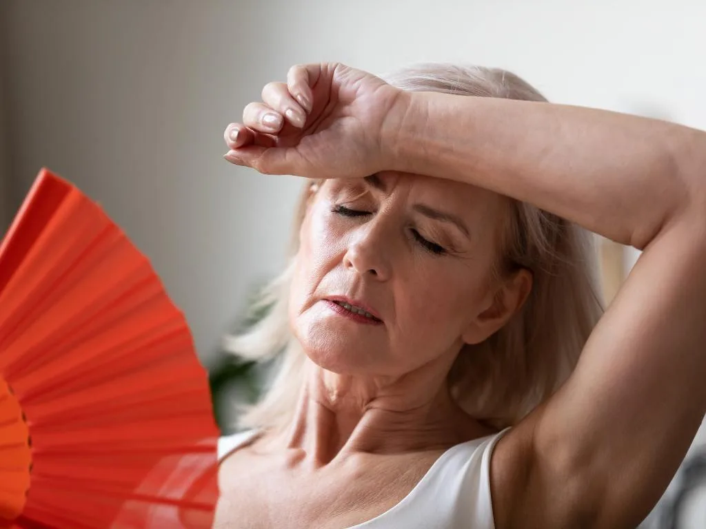 Mulher com calor se abanando com um leque por causa menopausa