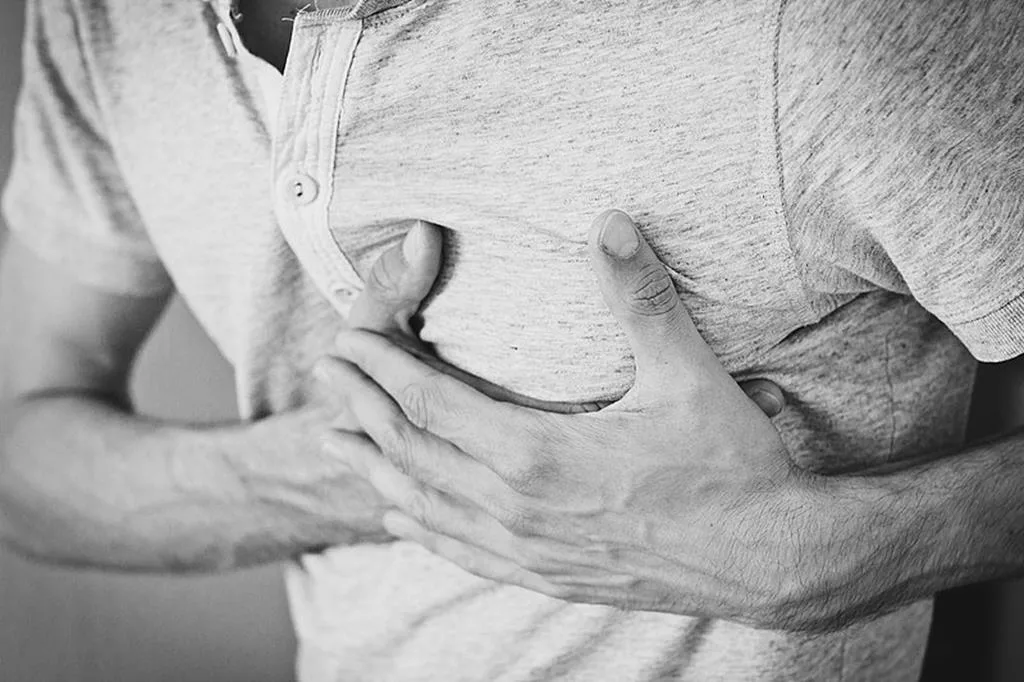 torso de um homem com as mãos no peito indicando problemas com os níveis de triglicérides