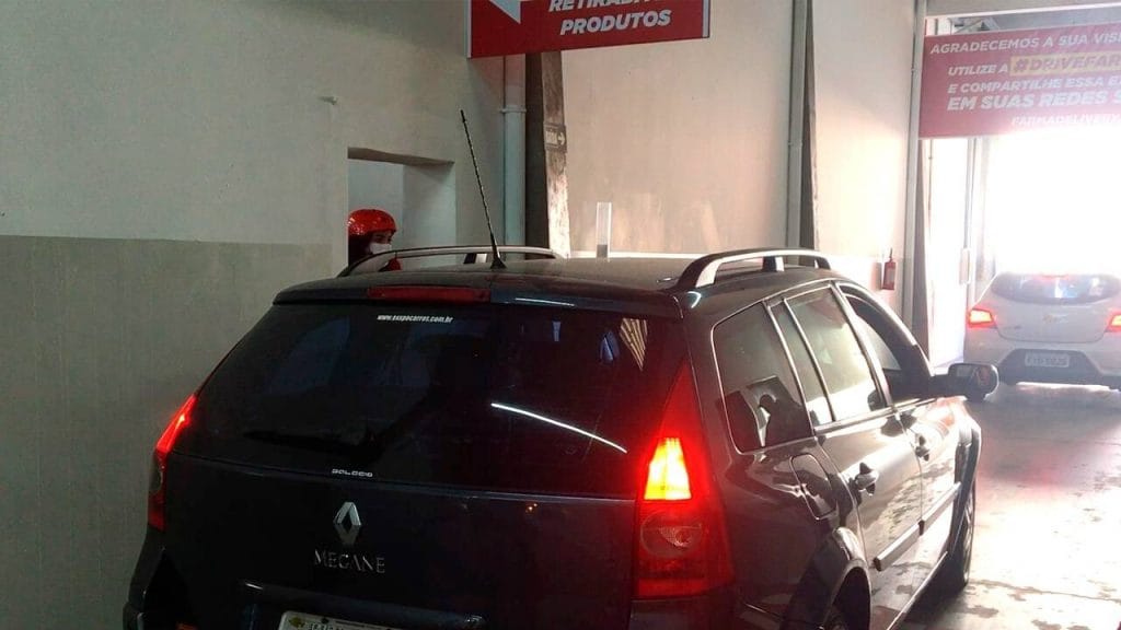 Carro parado em frente a cabine do Drive-in, funcionaria, com equipamentos de seguranças, realiza atendimento ao cliente.