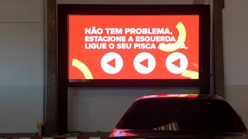 Carro estacionado em frente telão com informações sobre como realizar a compra no Drive-in Farmadelivery.
