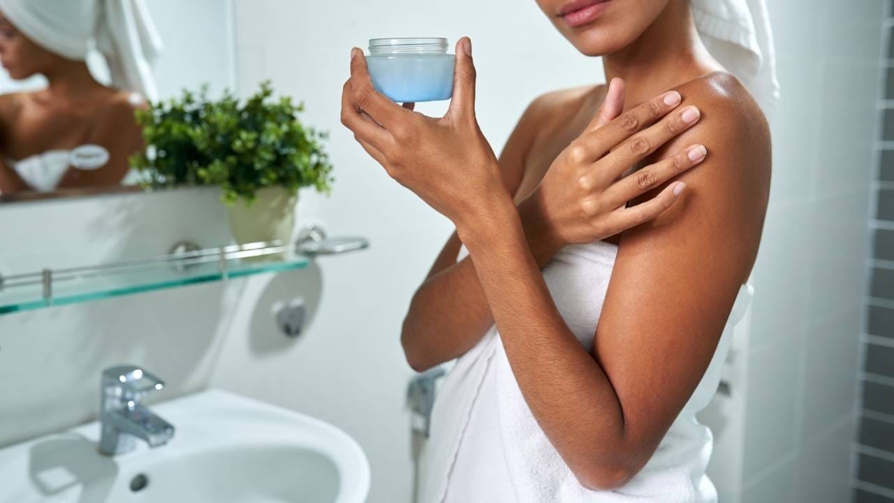 Mulher acaba de sair do banho, hidratando o corpo com produtos específicos para pele seca.
