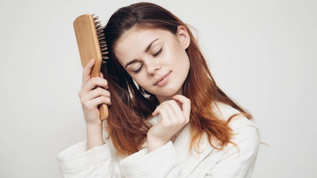 Mulher escovando os cabelos, com um rosto demonstrando tranquilidade.