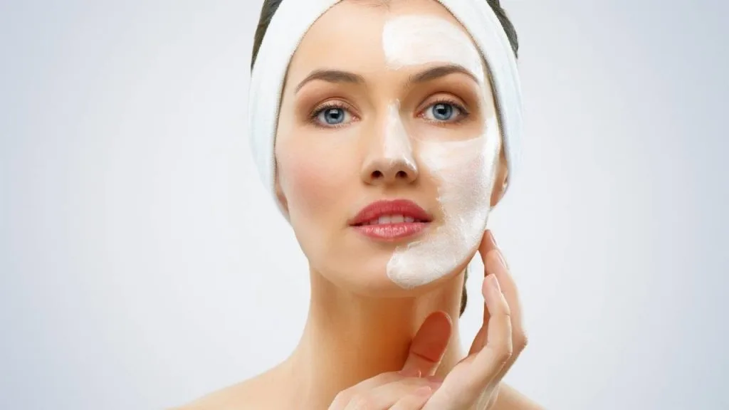 Mulher com metade da face coberta com hidratante.