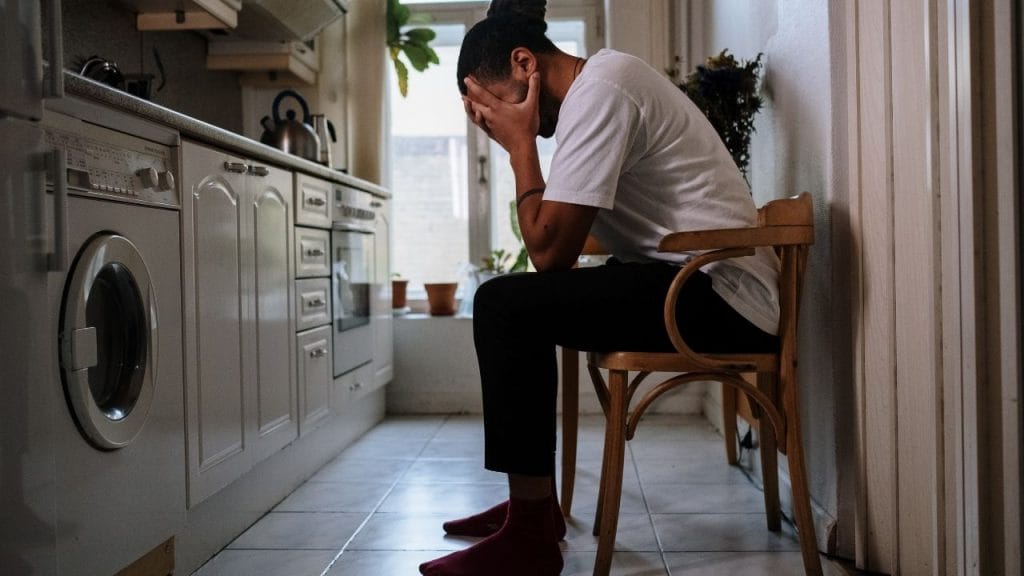 Homem sentado, com as mãos na cabeça, demonstrando certo tipo de aflição ou preocupação, causado pela saúde mental abalada.