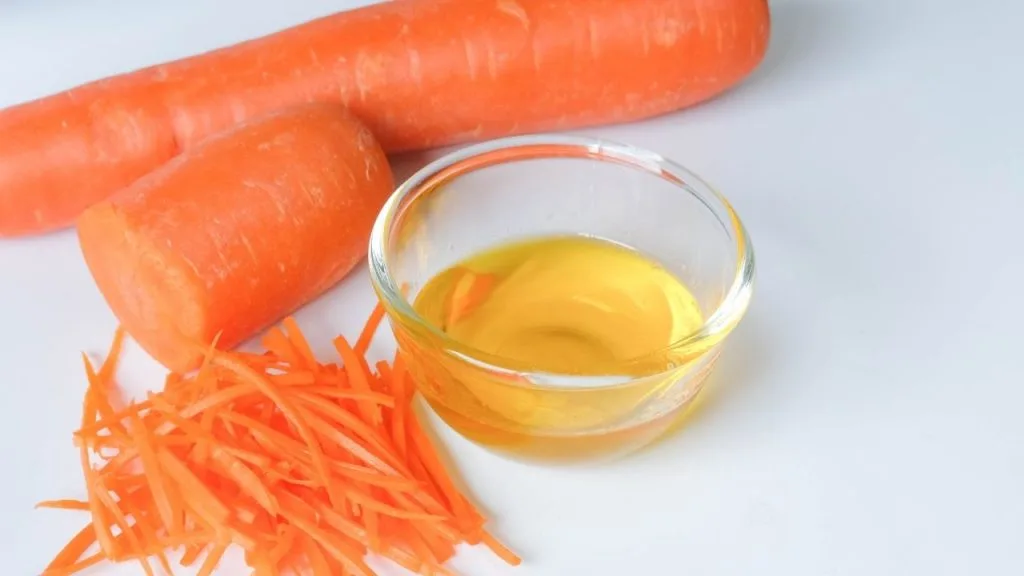 Na imagem, cenouras inteiras, em pedaços e ralada, ao lado de bowl contendo o óleo do alimento, utilizado no tratamento de cabelos com queda.