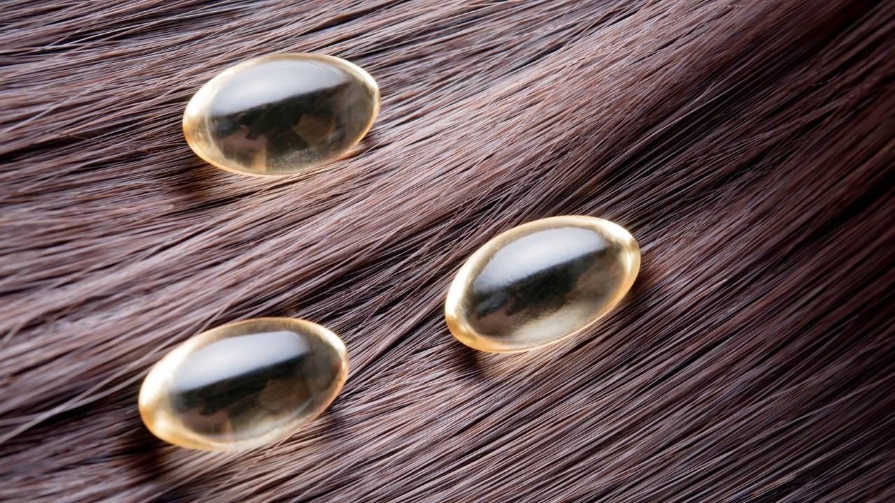 Na imagem, três capsulas de vitamina está sob cabelos.