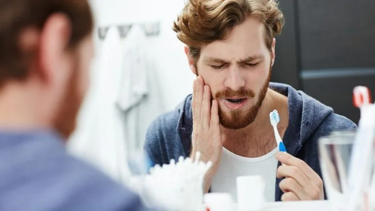 Homem demonstrando desconforto ao escovar os dentes.
