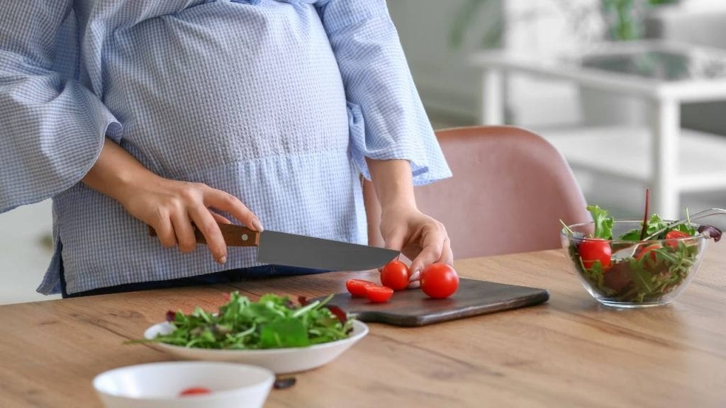 Gestante preparando uma salada com tomates, que ajudam a evitar estrias na gravidez.