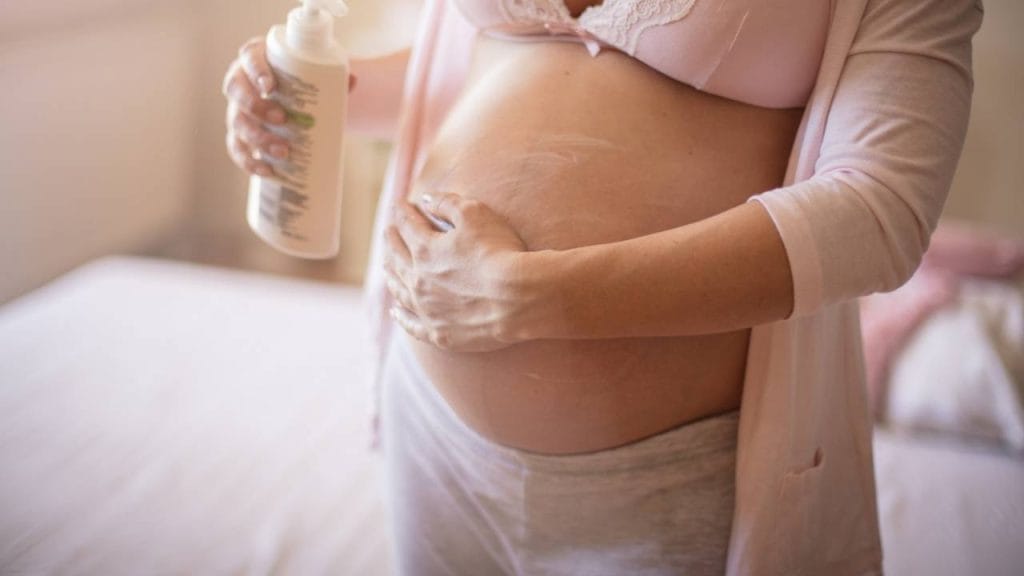 Gestante realizando massagem na barriga ao aplicar hidratante com ação antiestrias.