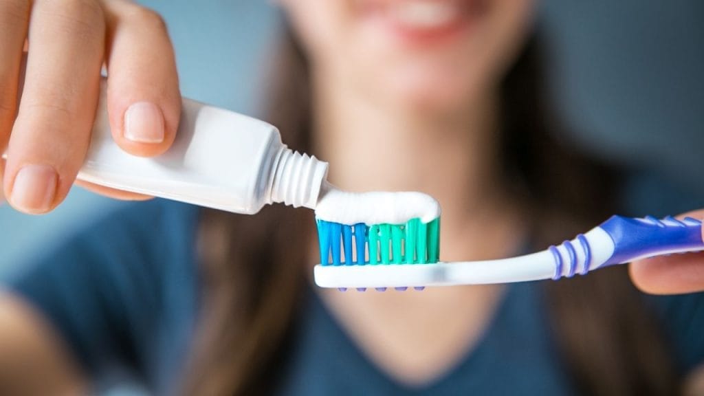 Mulher colocando creme dental na escova para realizar higiene bucal.
