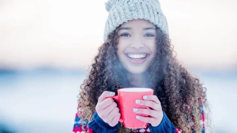 Mulher tomando chá e bem agasalhada seguindo dicas de saúde no inverno.