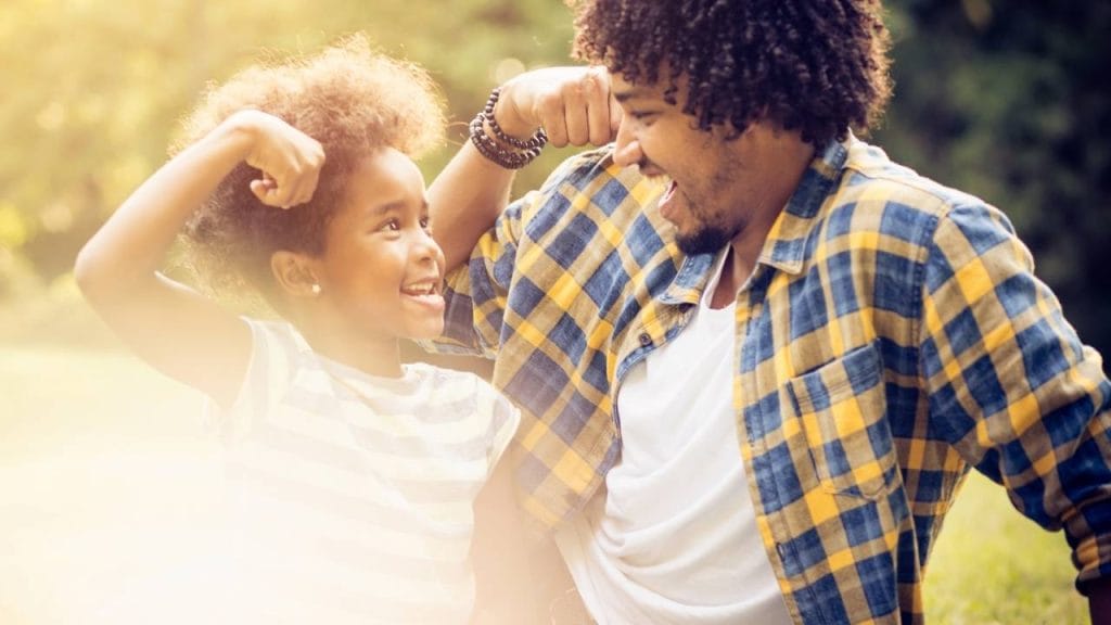 Criança e homem adulto sentados na grama demonstrando estarem fortes com o sistema imunológico alto.
