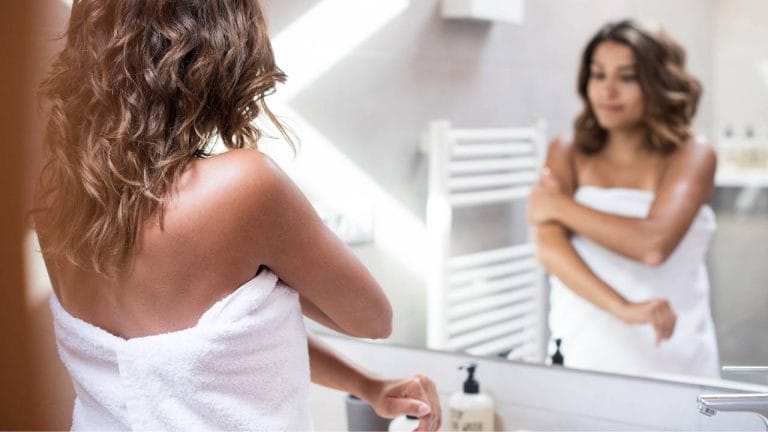Mulher após sair do banho, aplicando hidratante no corpo, para proteger a pele no inverno.