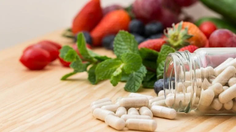 Imagem representando cápsulas de vitamina para aumentar imunidade e alguns alimentos ao fundo