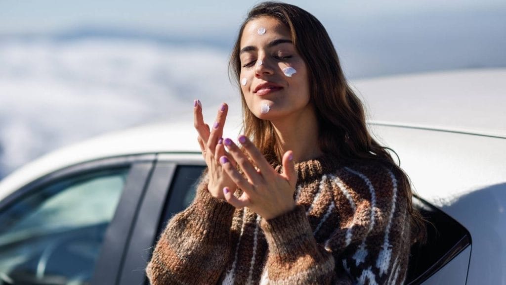 Mulher aplicando protetor solar no rosto, mesmo no inverno.