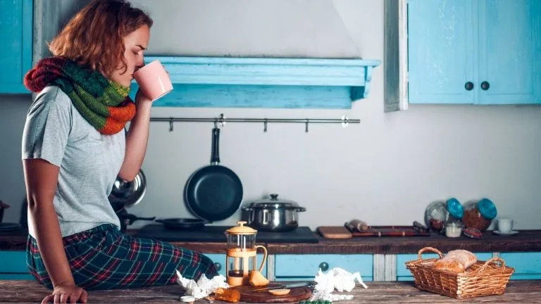 Mulher sentada na bancada da cozinha tomando remédio para tratamento da imunidade.