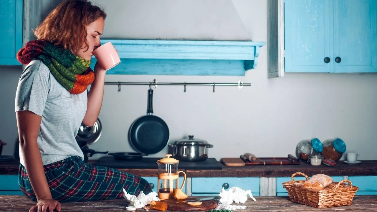 Mulher sentada na bancada da cozinha tomando remédio para tratamento da imunidade.