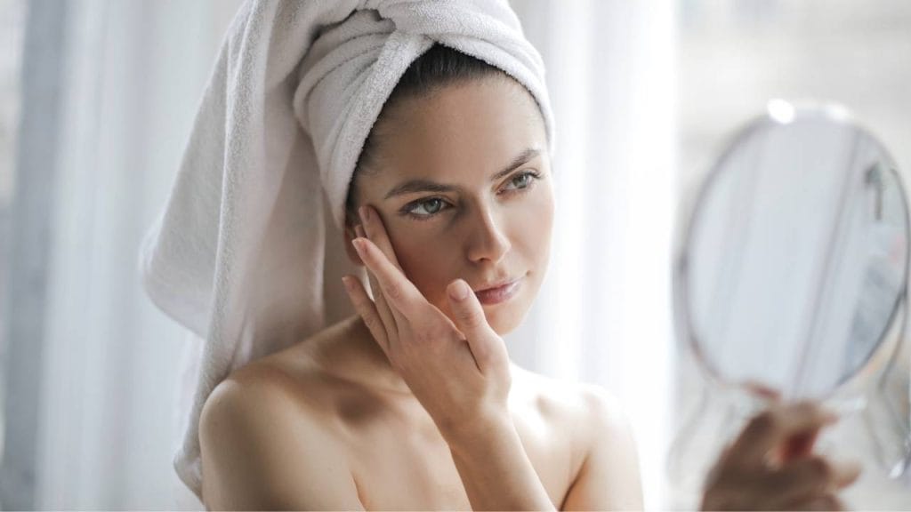 Mulher, após o banho analisando a pele do seu rosto.