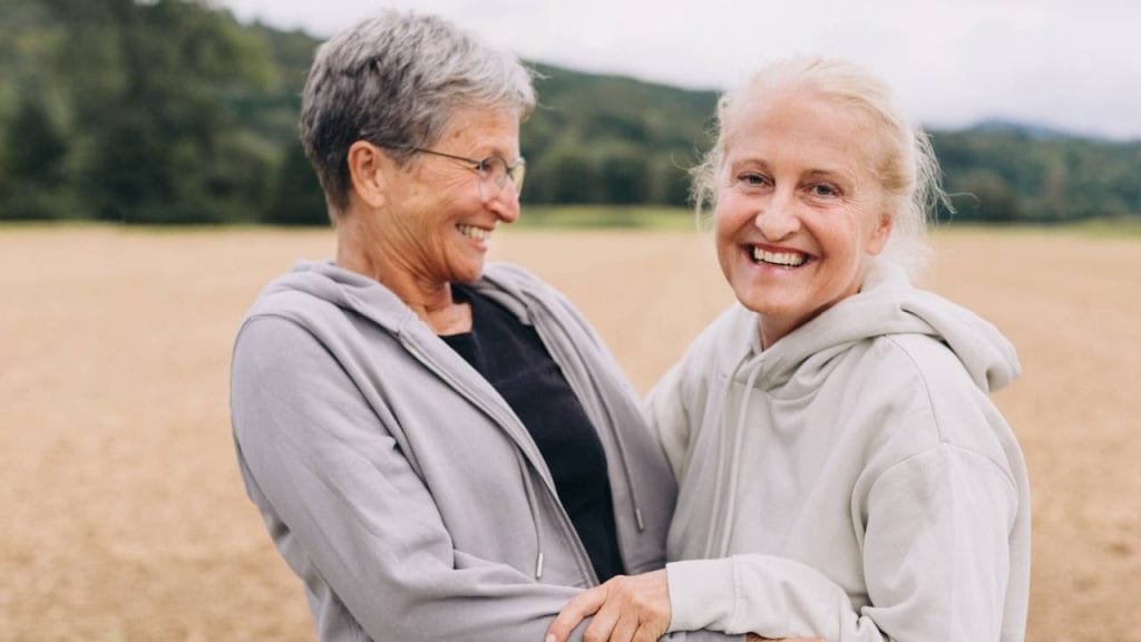 Duas mulheres abraçadas, dando risada, em meio a um campo.
