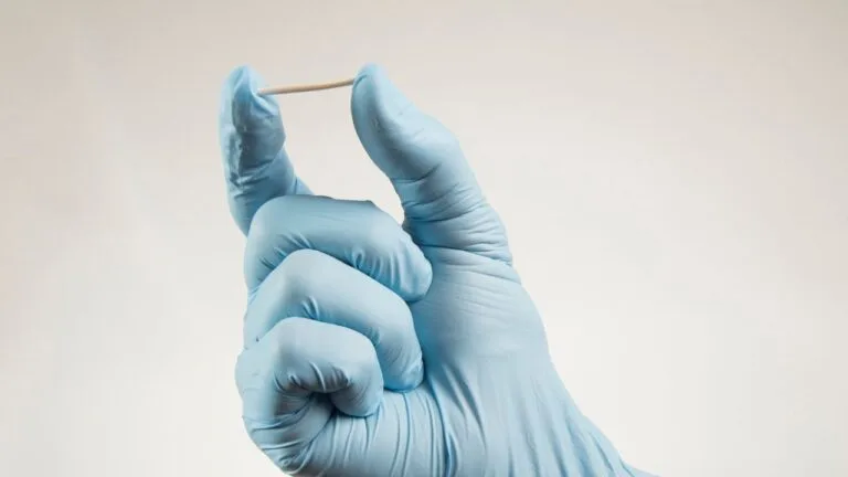 mão com luva azul segurando um implanon